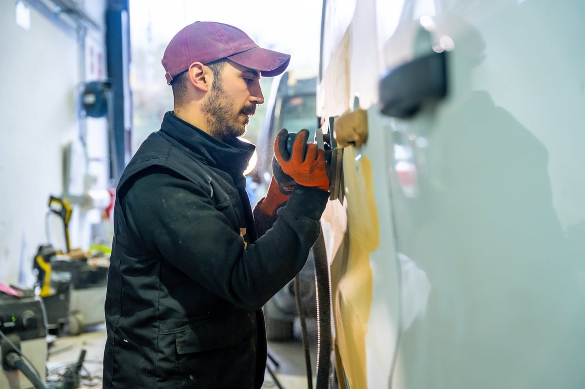 Auto body technician sanding a vehicle panel in a repair workshop