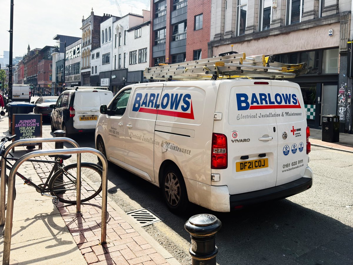 A service van with roof ladders parked on a busy UK high street